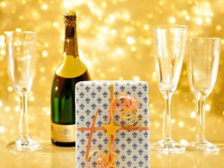 Festlich verpacktes Geschenk mit Ribbclip neben Sektflasche und Gläsern